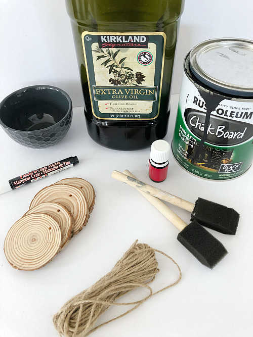 Items needed to make scented wood slice ornaments: chalkboard paint, wood slices, twine, oil, and essential oil