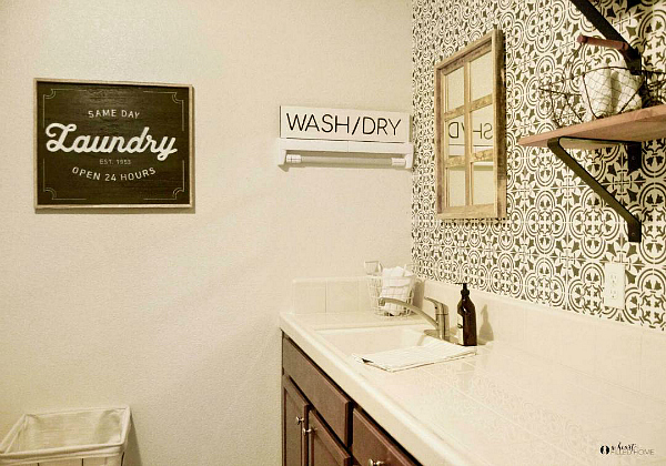 Laundry room makeover for $100 featuring a stenciled wall, new shelving, and laundry signs hung on the wall.