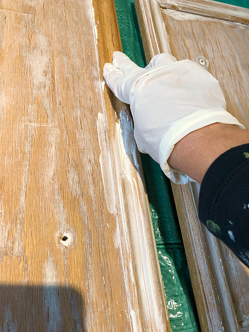 Applying joint compound to trim of cabinet door using gloved fingers