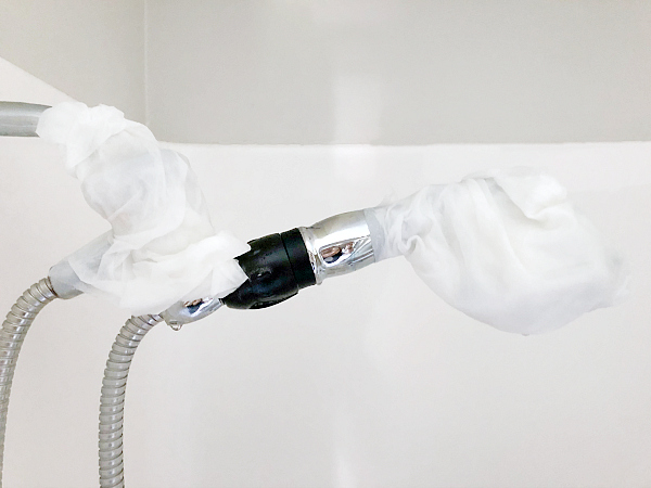 Vinegar soaked paper towels are wrapped around the shower head and handle in order to clean shower head