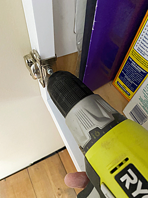 Removing hardware with a drill prior to painting laminate cabinets.