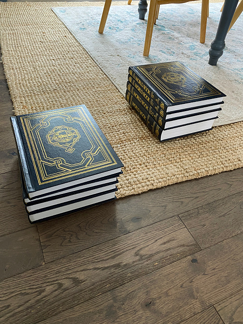 Heavy object (in this case a stack of encyclopedias) sitting on the corners of a curling rug to weigh it down.