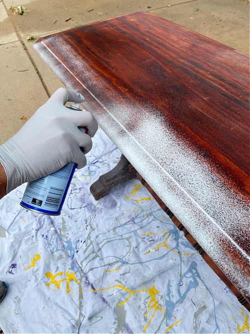 Spraying oven cleaner on furniture to strip the stain