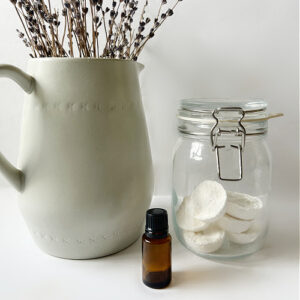 DIY Shower Steamers in Jar next to bottle of essential oil and vase of lavender