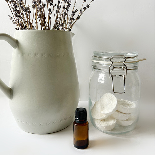 DIY Shower Steamers in Jar next to bottle of essential oil and vase of lavender