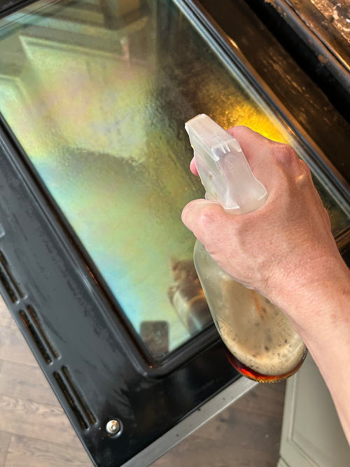 Spraying black tea glass cleaner on oven door after cleaning with pumice stone