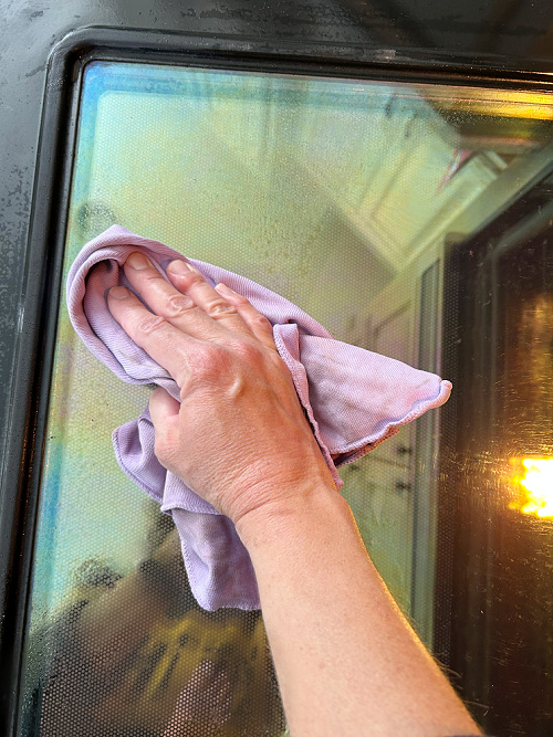Using window cloth to clean oven door after spraying with glass cleaner