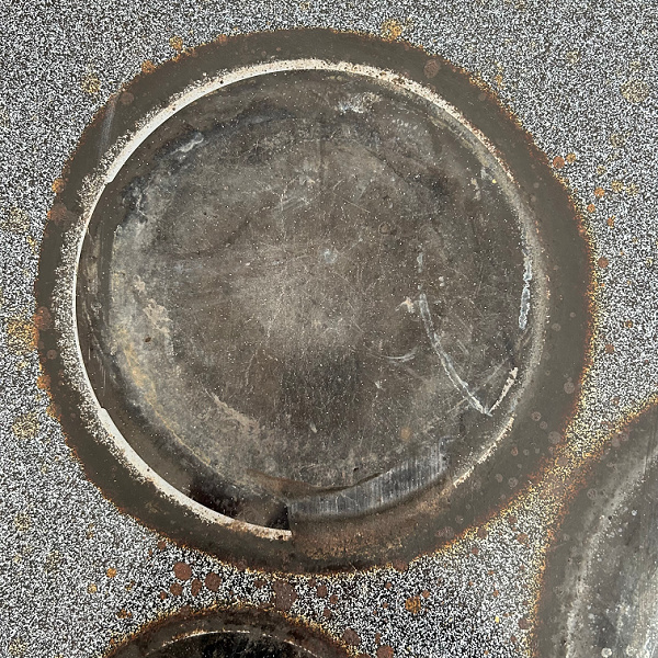 Burner on glass stovetop with large black rim of burnt on food