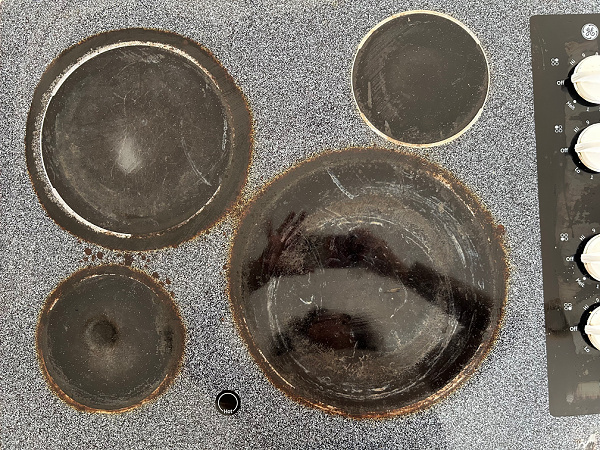 Glass stovetop showing burnt on mess around all burners