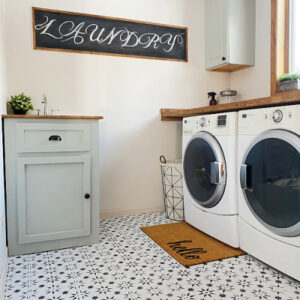 Laundry room with stenciled floor, white washer and dryer with a little sage green utility sink
