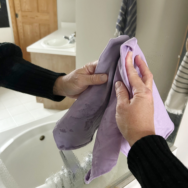 Wiping mirror with cloth after spraying black tea glass cleaner